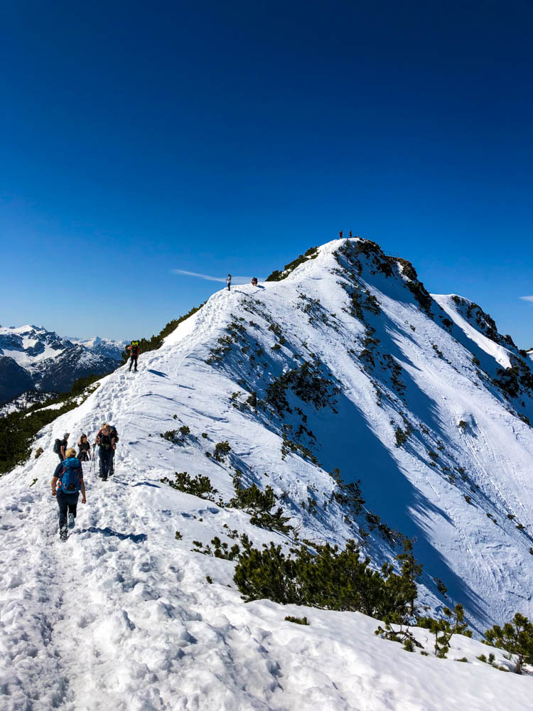 Julian auf einem schneebedeckten Grat von Herzogstand zum Pavilion. Der Himmel ist strahlend blau und der Schnee leuchtet weiß von der Sonne in den Alpen.