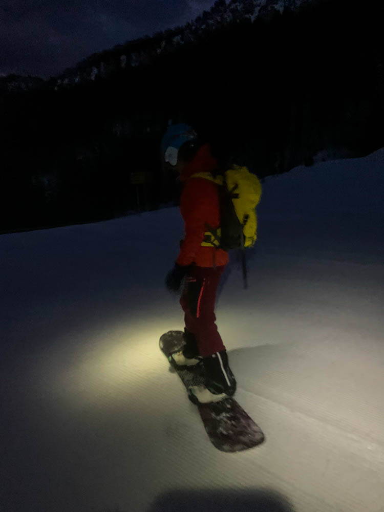 Abfahrt im Dunkeln. Melanie steht auf ihrem zusammengebauten Splitboard (jetzt wieder Snowboard) und um sie herum ist es schwarz von der Nacht.