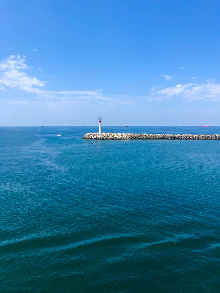 Hafenausfahrt in Huelva. Auf der Hafenmauer steht ein kleiner Leuchtturm. Dahinter ist der scheinbar unendliche Atlantik zu sehen.