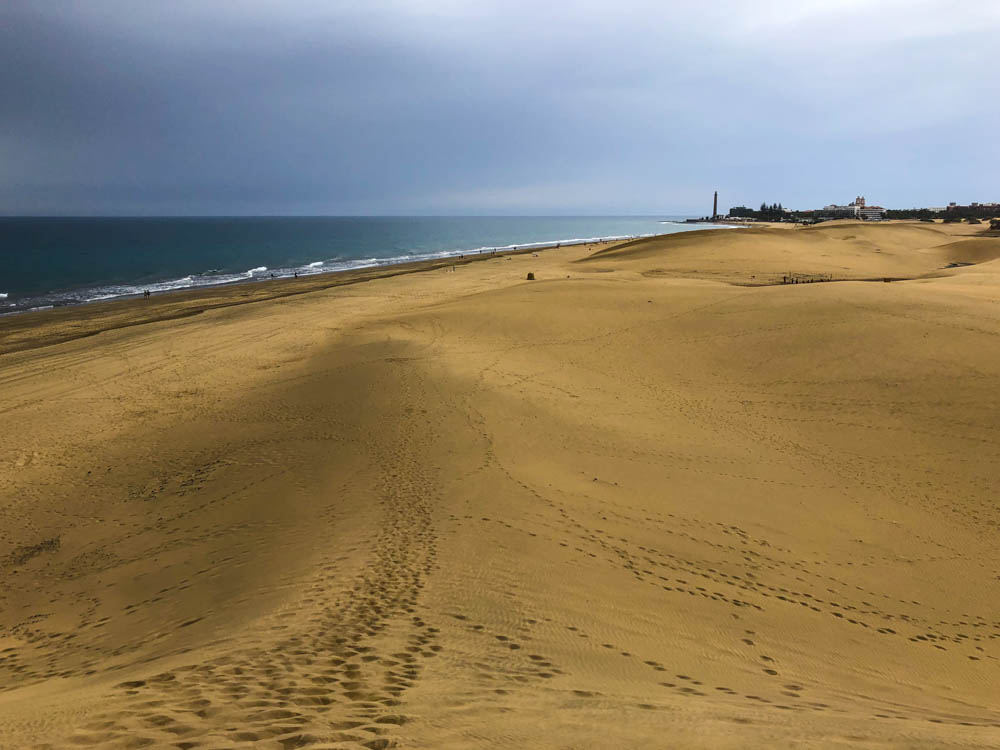 Blick von einem Hügel in den Dünen von Maspalomas. Es ist der Strand, der Ozean und der Leuchtturm von Maspalomas zu sehen.