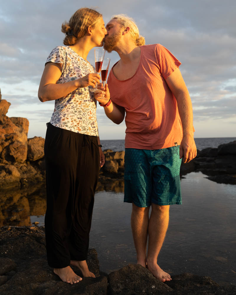 Melanie und Julian stehen am Atlantik und Küssen sich in der Abendsonne. Dabei halten sie ihre Sektgläser in der Hand uns stoßen auf das Divemaster Praktikum an.