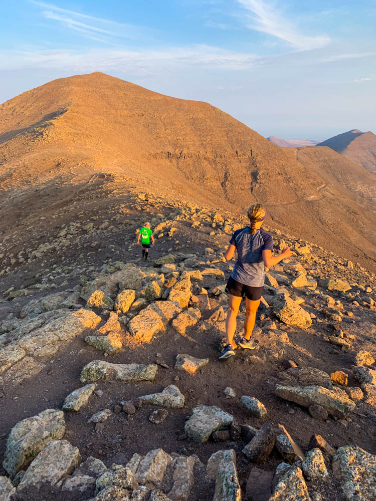 Melanie beim Trail Running auf einem Grat mit Abendsonne. Joggend Fuerteventura entdecken bei leichten Schleierwolken und bergiger Landschaft