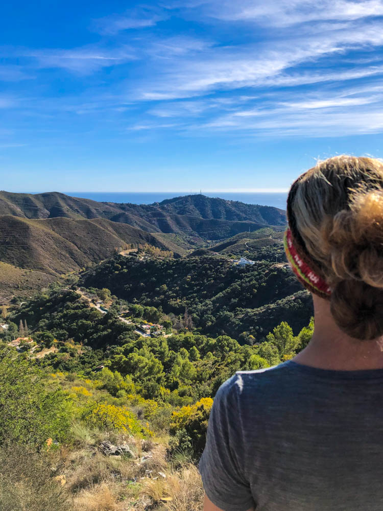Melanie blickt von einem Aussichtspunkt auf einem Berg auf eine Hügellandschaft in Andalusien. Am Horizont ist das Mittelmeer zu sehen. Rückfahrt über Spanien durchs Landesinnere