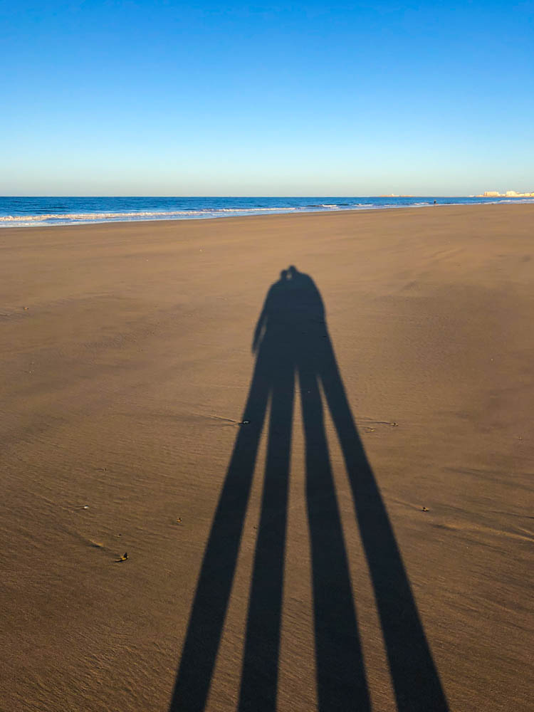 Melanie und Julian als Schattenbilder im Strand von Cadiz. Der Himmel ist strahlend blau und der Atlantik ist zu sehen.