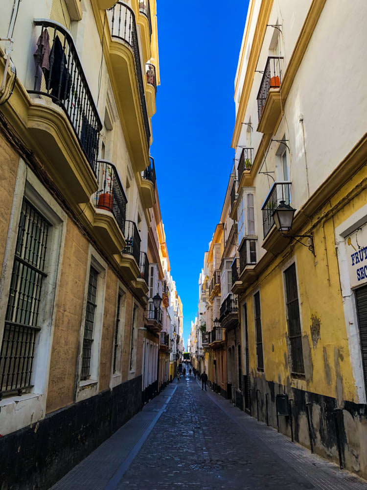 Landestypische Straße in der Innenstadt von Cadiz. Es sind rechts und links die Häuserfronten zu sehen, in der Mitte der strahlend blaue Himmel.