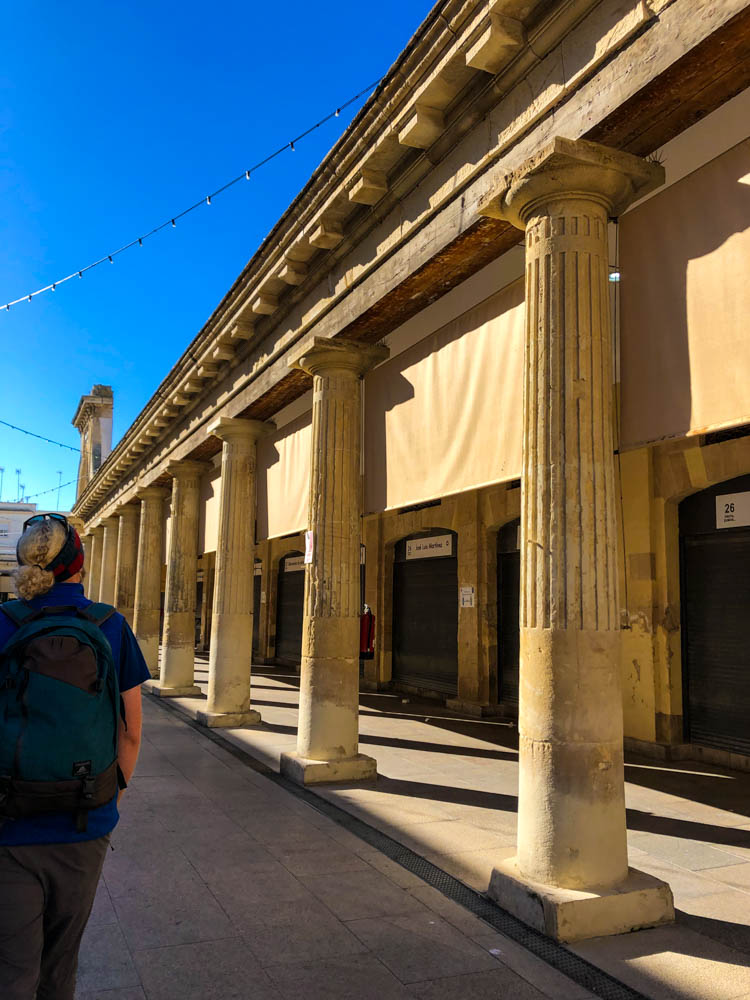 Julian läuft über den Markt von Cadiz. Es ist ein Gebäude auf Säulen zu sehen, sowie der blaue Himmel.