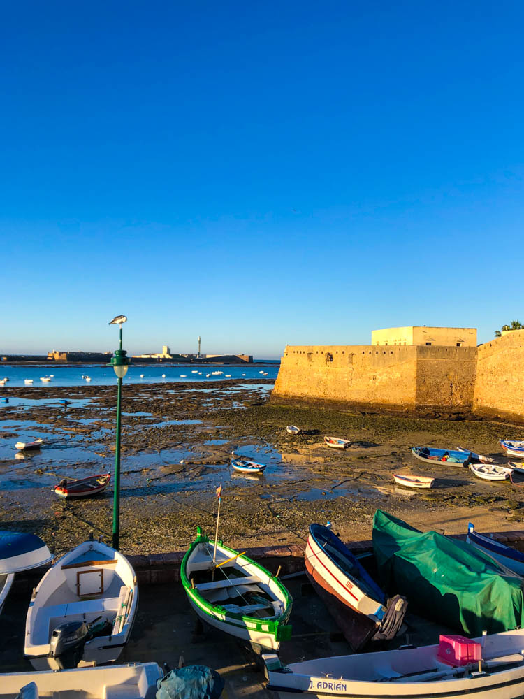 Es ist Ebbe in Cadiz und die im Hafen liegenden Boote sind auf Grund gelaufen. Zudem ist die Hafenmauer zu sehen. Der Himmel ist strahlend blau. Rückfahrt über Spanien - erster Stopp: Cadiz