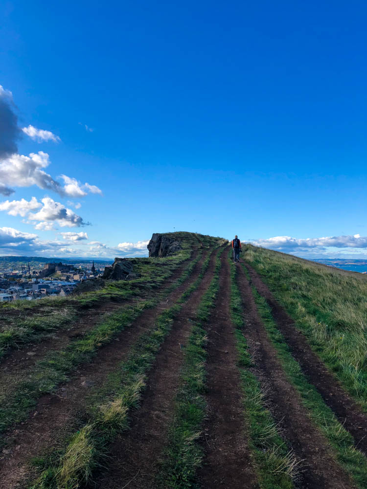 Arthur's Seat Edinburgh - klassische Stadtbesichtigung. Julian wandert auf einer Anhöhe, der Himmel ist strahlend blau.