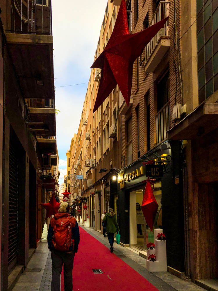 Julian läuft auf einem roten Teppich, welcher in einer der Straßen in Murcia ausliegt. Es hängen Sterne als Weihnachtsdekoration zwischen den Häusern. Rückfahrt über Spanien - Murcia