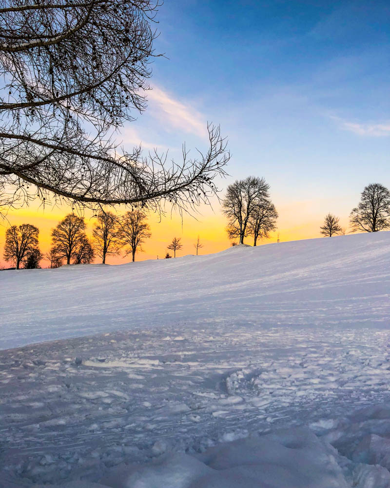 Sonnenuntergang am Ende einer tollen Splitboardtour bei Nesselwang. Der Himmel leuchtet teils orange teils blau und im Vordergrund ist die Schneelandschaft zu sehen. Winter in den Alpen - Nesselwang