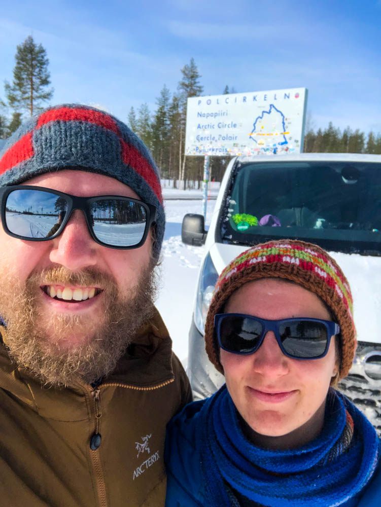 Selfie von Melanie, Julian und Van Vivaldi vor Polarkreis Schild in Schweden. Es herrschen winterliche Bedingungen, der Himmel ist blau - Fahrt in den hohen Norden