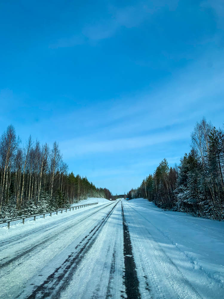 Die Fahrbahn ist teilweise mit Schnee bedeckt, der Himmel ist blau - Fahrt in den hohen Norden Schweden