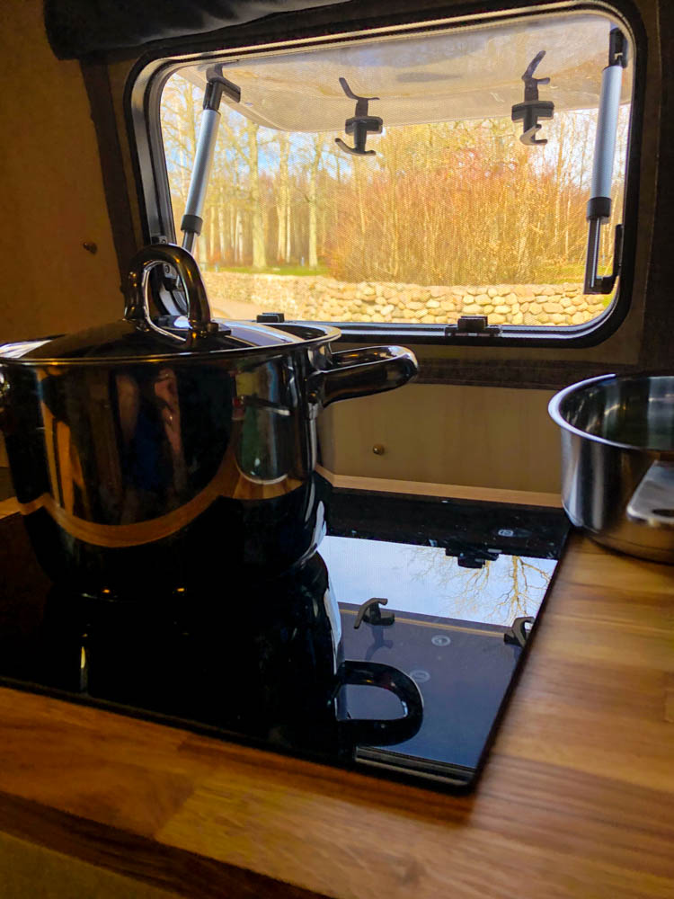 Küche in Van Vivaldi mit Ausblick aus dem Fenster auf Waldstück. Fahrt in den hohen Norden über Schweden
