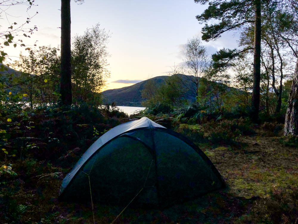 Zelt in einem Waldstück am See aufgebaut. Trekking West Highland Way Schottland. Sonnenuntergang