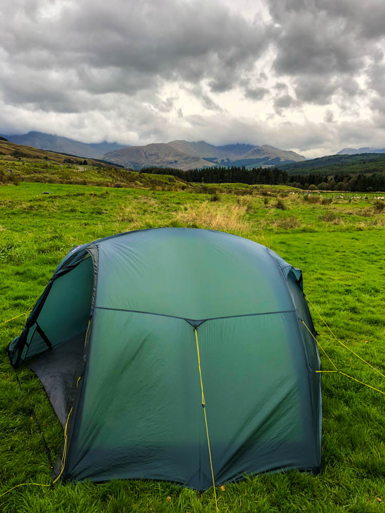 Zelt aufgebaut auf einer Wiese. Der Himmel ist sehr bewölkt. West Highland Way Trekking Schottland