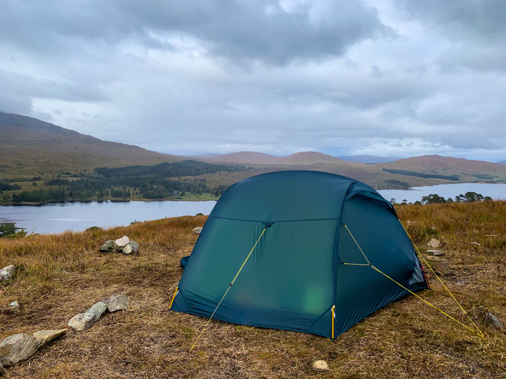 Aufgebautes Zelt auf einem Hügel mit Blick auf einen See und schottische Highlands. Trekking West Highland Way Schottland