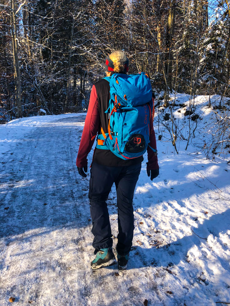 Julian beim Wandern in Kempten. Er läuft auf eisigen Schneeflächen in einem Wald. Winter in den Alpen - Kempten