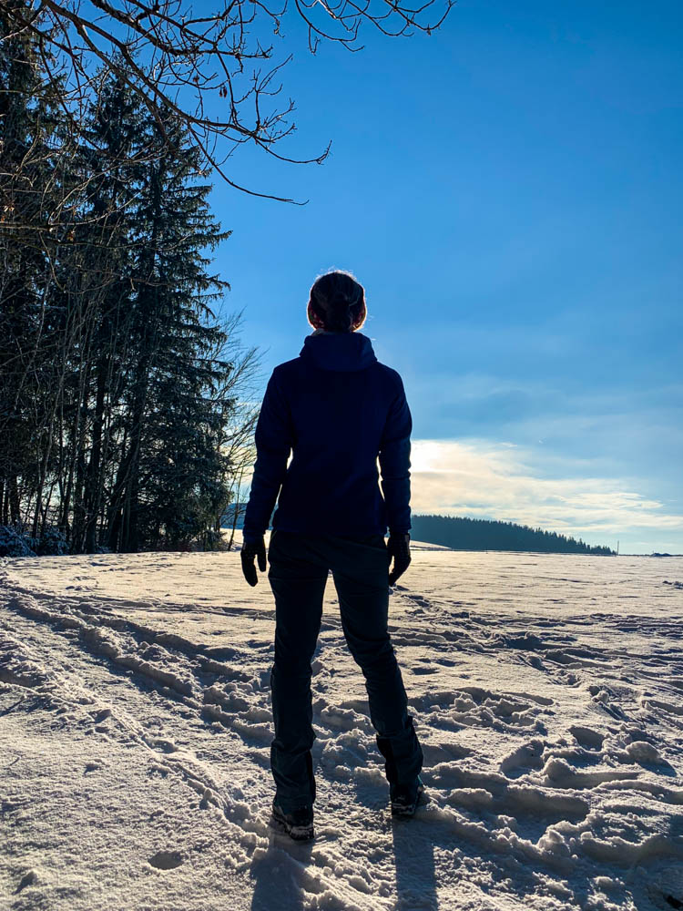 Melanie beim Wandern bei Kempten im Winter. Die Schneelandschaft und der blaue Himmel strahlen um die Wette. Mittendrin Melanie - Winter in den Alpen