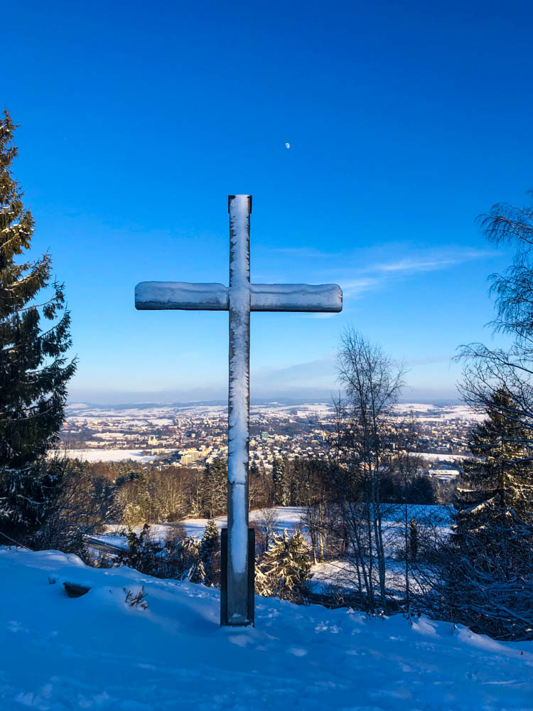 Kreuz auf einem Hügel bei Kempten in Winterlandschaft. Der Himmel ist kräftig blau.
