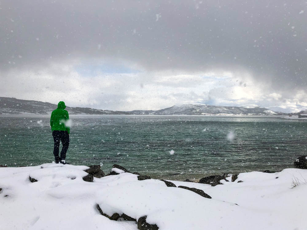 Julian blickt auf den Atlantik und steht dabei im Schnee. Es schneit zudem kräftig. Nordnorwegen Anfang April