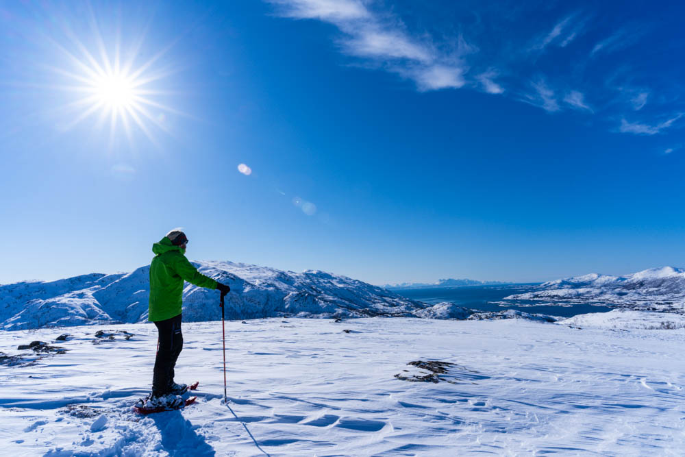 Schneeschuhwanderung Nordnorwegen Anfang April. Julian blickt auf die verschneite Berglandschaft. Es ist ein Sonnenstern zu sehen, der Himmel ist kräftig blau.