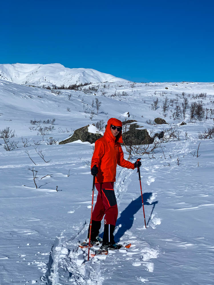 Schneeschuhwanderung Nordnorwegen Anfang April. Melanie blickt in die Kamera, hinter ihr ist die verschneite Berglandschaft, der Himmel ist kräftig blau.
