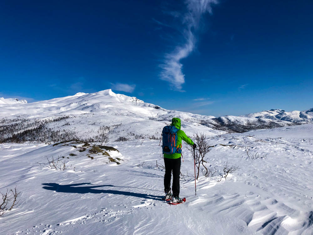 Schneeschuhwanderung Nordnorwegen Anfang April. Julian blickt auf die verschneite Berglandschaft, der Himmel ist kräftig blau.