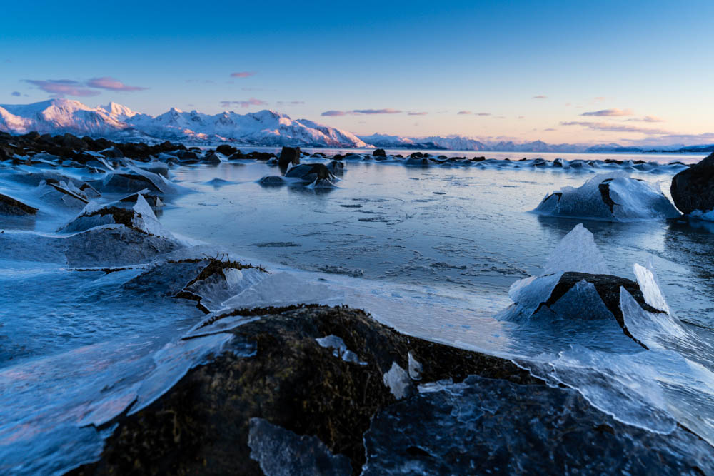 Zersprungene Eisflächen auf dem See, herrliche Eislandschaft beim Atlantik bei Sortland. Bergpanorama im Hintergrund vom Sonnenuntergang beleuchtet. Nordnorwegen Anfang April