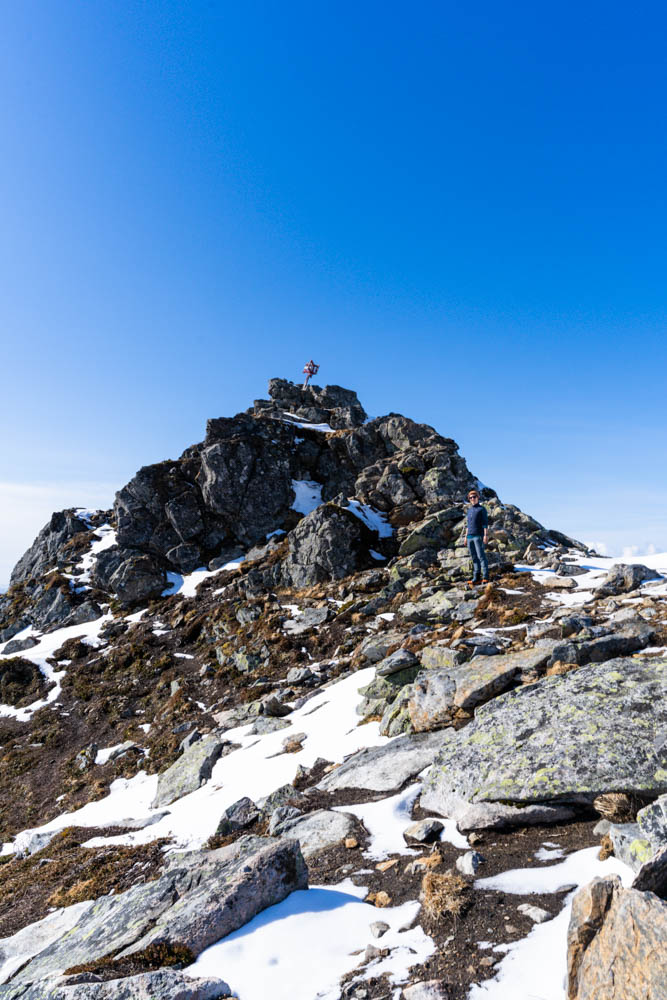 Gipfelkreuz des Festvågtinden bei Henningsvaer. Der Himmel ist strahlend blau, es liegt ein wenig Schnee vor dem Gipfel.