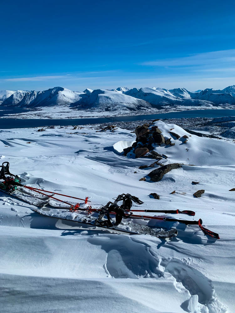 Die Splitboards liegen nach Aufstieg im Schnee, im Hintergrund ist eine Berglandschaft sowie Sortland im Tal zu sehen. Splitboarding Nordnorwegen Anfang April