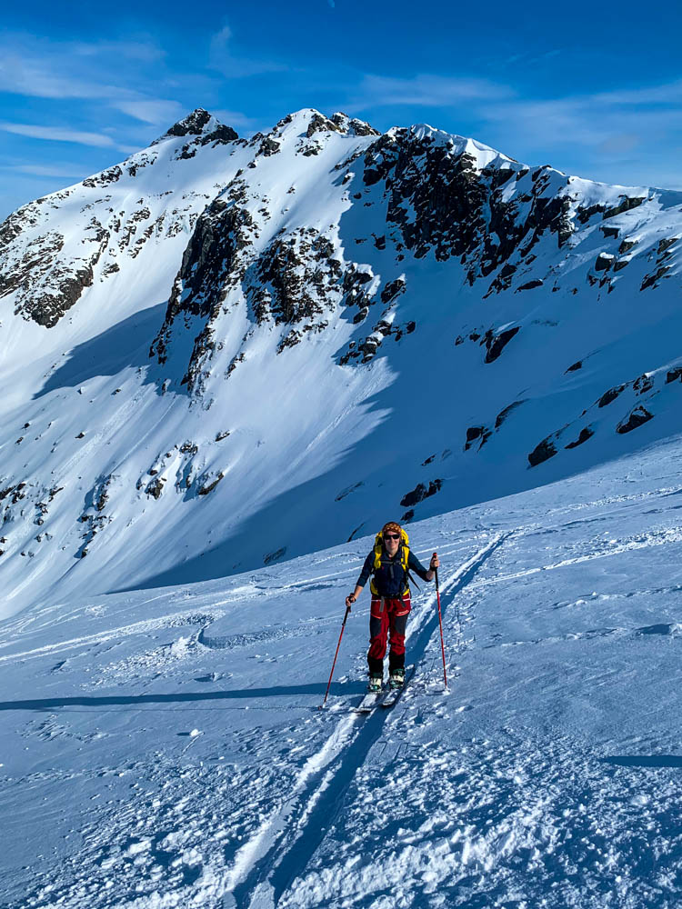 Melanie beim Aufstieg mit ihrem Splitboard auf den Lofoten im April am Rundfjellet. Der Himmel strahlt kräftig blau, schöner Kontrast zu dem restlichen weiß der Berge und Piste.