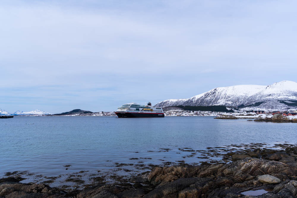 Hurtigruten Schiff läuft im Fjord bei Stokmarknes ein. Die Bergkulisse im Hintergrund ist schneebedeckt - Nordnorwegen Anfang April