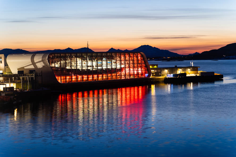 Abenddämmerung in Stokmarknes Anfang April Nordnorwegen. Auf dem Bild ist das Hurtigruten Museum zu sehen, welches abends beleuchtet wird. Die Bergkulisse im Hintergrund leuchtet noch orange.