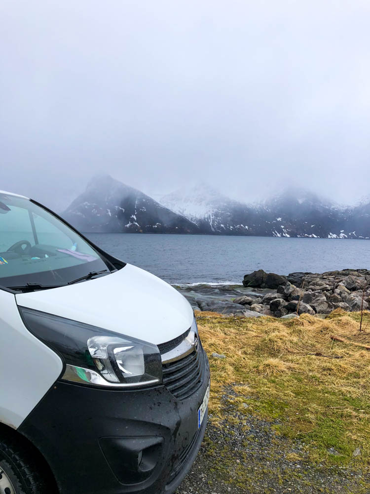 Van Vivaldi steht am Europäischen Nordmeer, verschneite in Nebel verhangene Gipfel sind auf der anderen Seite des Fjords zu sehen. Tour Norwegen - über Senja nach Tromsö