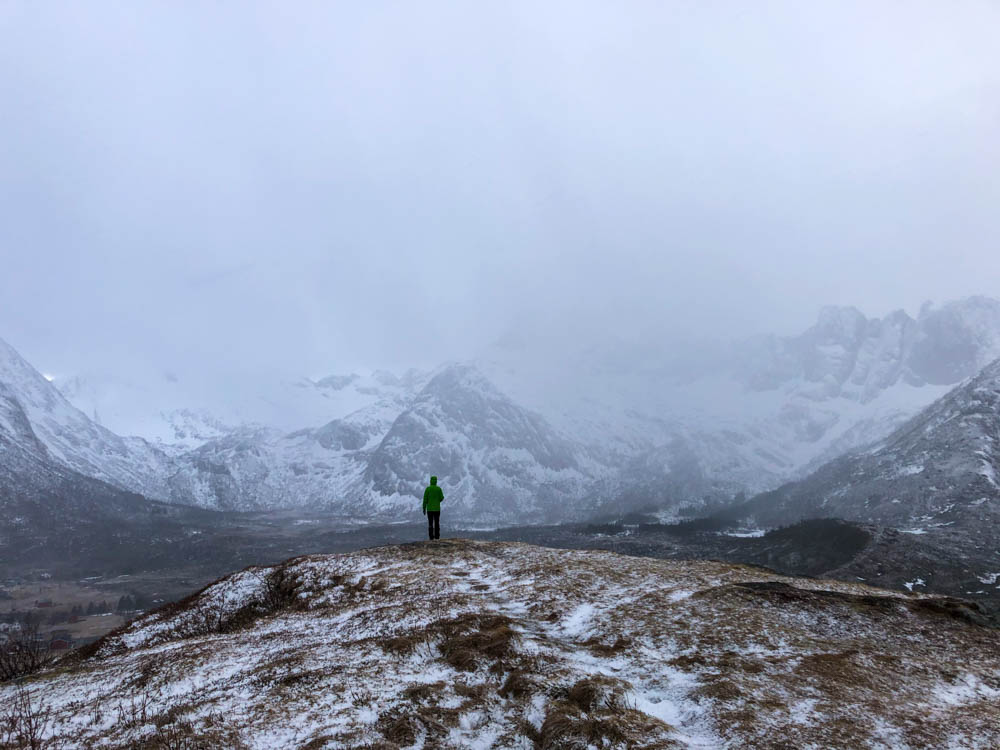 Julian steht auf Gipfel Knuten Senja. Er blickt auf die verschneite Berglandschaft, welche gerade im Nebel hängt. Tour Norwegen - über Senja nach Tromsö