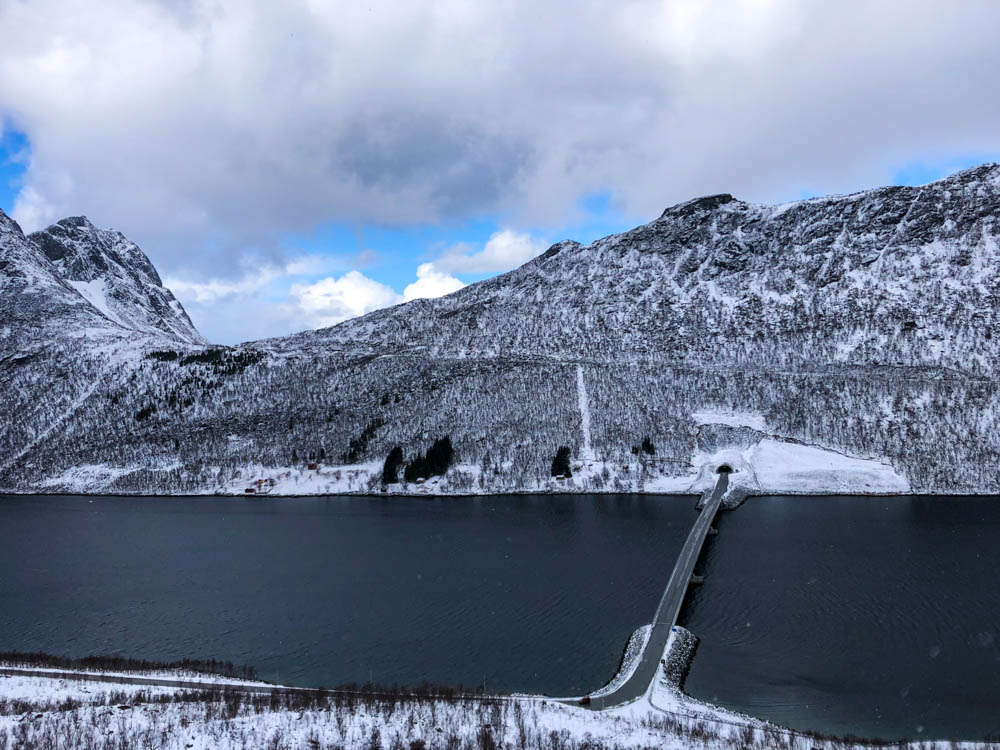 Verschneite Berglandschaft Senja - Blick von Anhöhe auf eine Brücke, die über einen Fjord führt.