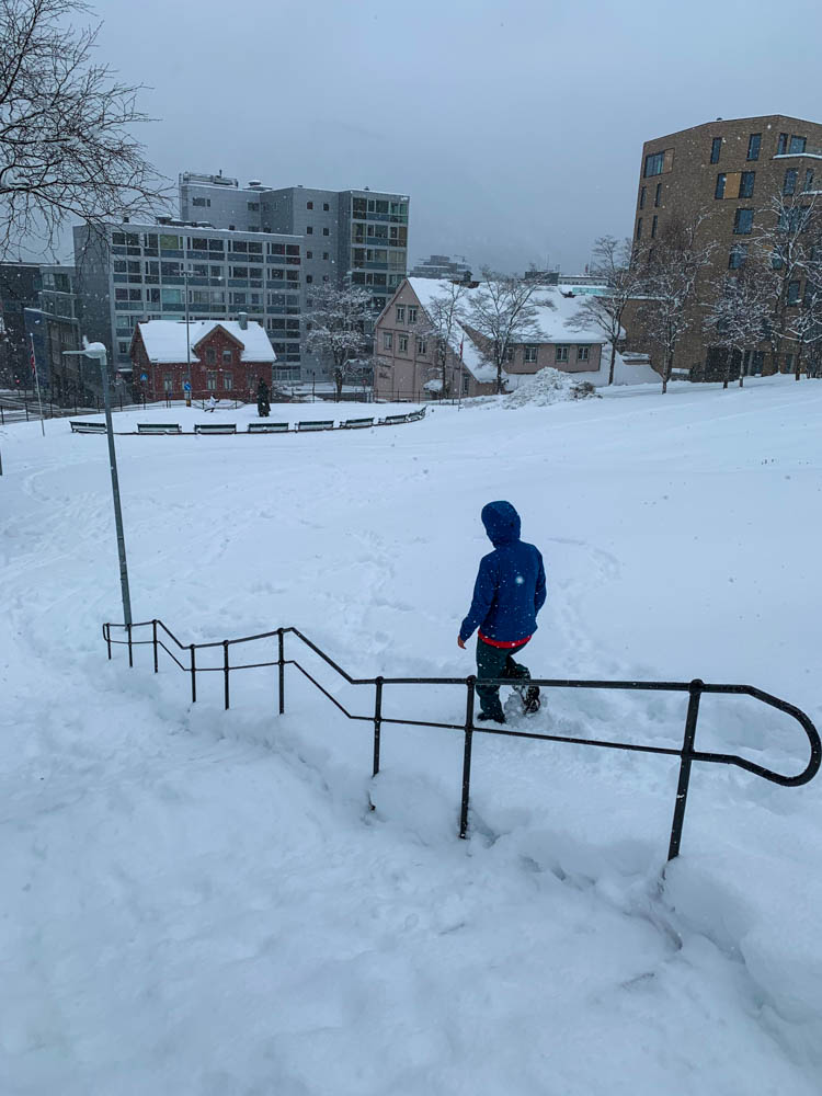 Melanie läuft im Schnee in Tromsö einen Hang hinab. Die Treppe daneben lässt sie links liegen, da diese sehr rutschig ist. Über Senja nach Tromsö - Schnee ohne Ende