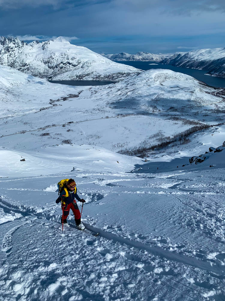 Melanie im Aufstieg zum Gipfel Steinskarstinden. Im Hintergrund ist die verschneite Berglandschaft Norwegens zu sehen sowie ein Fjord.