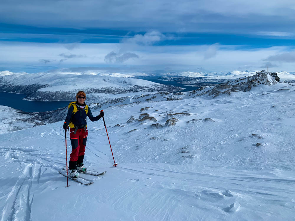 Melanie mit Splitboard auf dem Weg zum Gipfel vom Steinskarstinden. Im Hintergrund sind Fjorde sowie eine verschneite Berglandschaft zu sehen. Über Senja nach Tromsö - Schnee ohne Ende