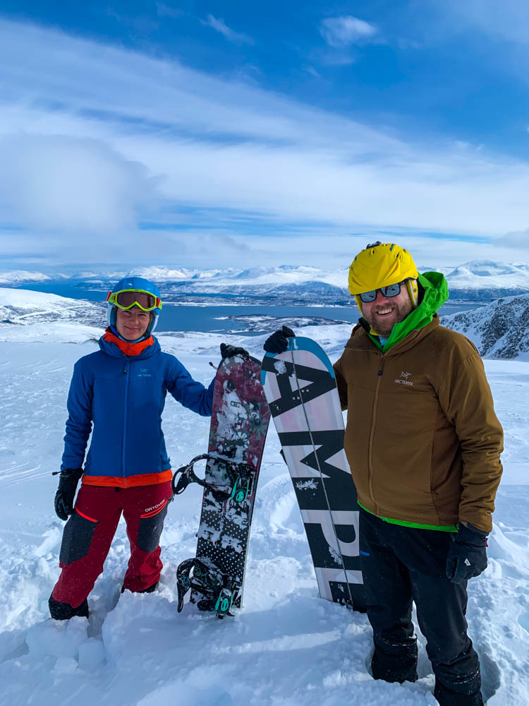 Melanie und Julian stehen auf dem Gipfel vom Steinskarstinden und stützen sich auf ihrem zusammengebauten Splitboard. Hinter ihnen ist eine verschneite Berglandschaft zu sehen.