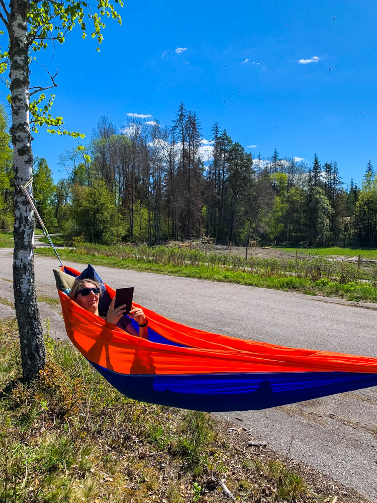 Melanie liegt in Schweden in einer Hängematte, welche zwischen zwei Bäumen gespannt ist, und liest ein Buch. Der Himmel ist strahlend blau.