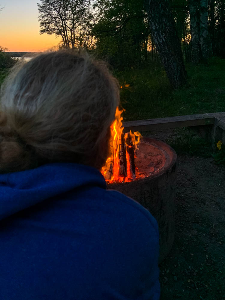 Lagerfeuer in Schweden bei Sonnenuntergang. Julian sitzt im Vordergrund, die Flamme direkt vor ihm