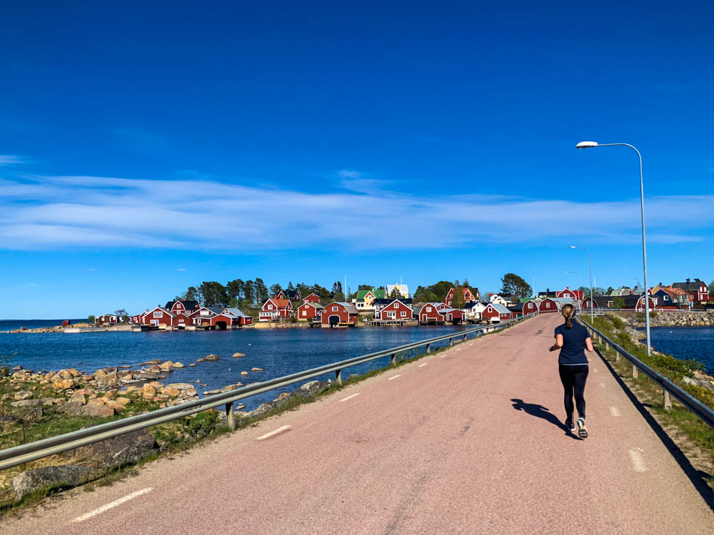 Melanie beim Joggen in Schweden. Sie läuft gerade über eine Brücke auf eine Insel mit vielen kleinen, roten Häusern. Der Himmel ist kräftig blau.