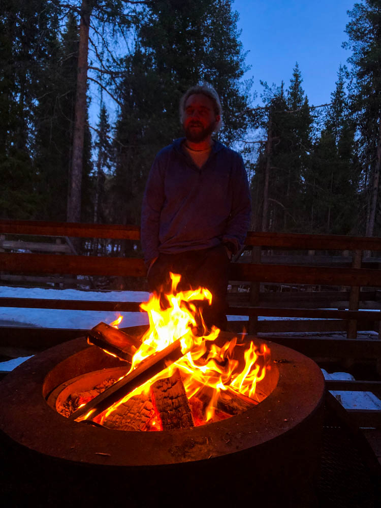 Julian steht neben einem Lagerfeuer im Muddus Nationalpark in Nordschweden. Es ist Frühling und mitten in der Nacht immer noch nicht richtig dunkel.