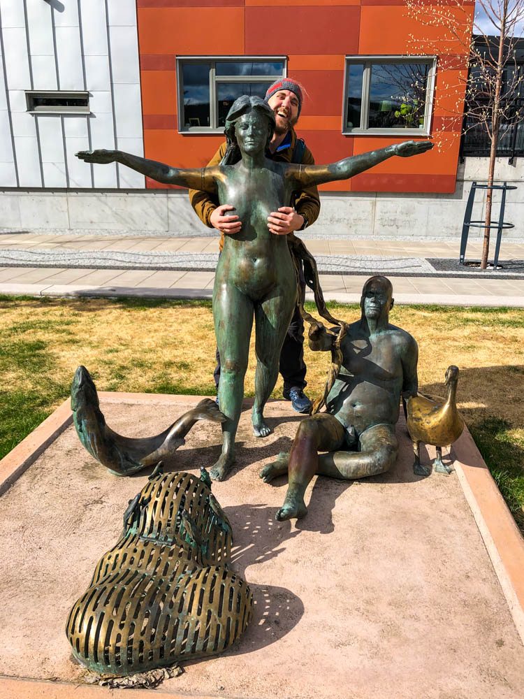 Julian steht hinter einer weiblichen Statue in Sundsvall Schweden und bedeckt mit seinen Händen die Brüste