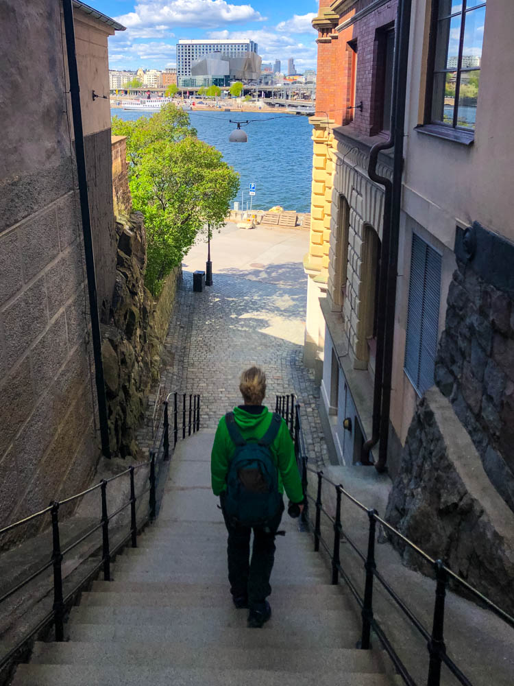 Julian läuft eine Treppe in Stockholm herunter. Es ist vor ihm ein Fluss zu sehen sowie die gegenüberliegende Stadtseite.