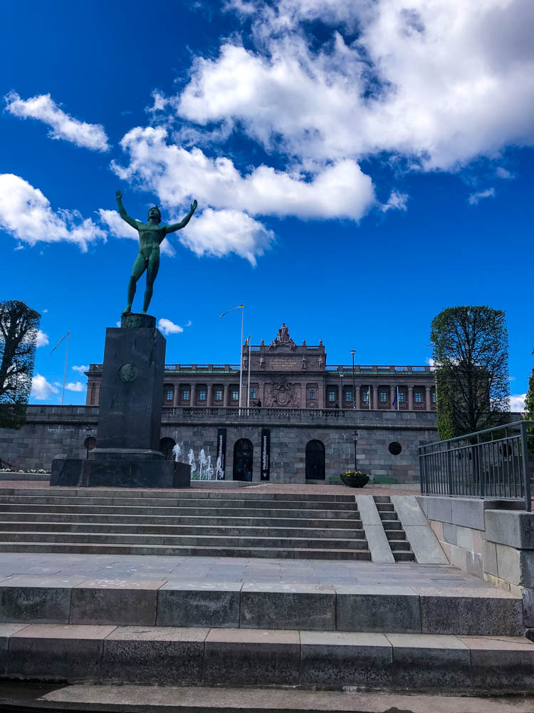 Parlament in Stockholm im Hintergrund des Bildes zu sehen, im Vordergrund ist eine Statue und ein paar Wasserspiele
