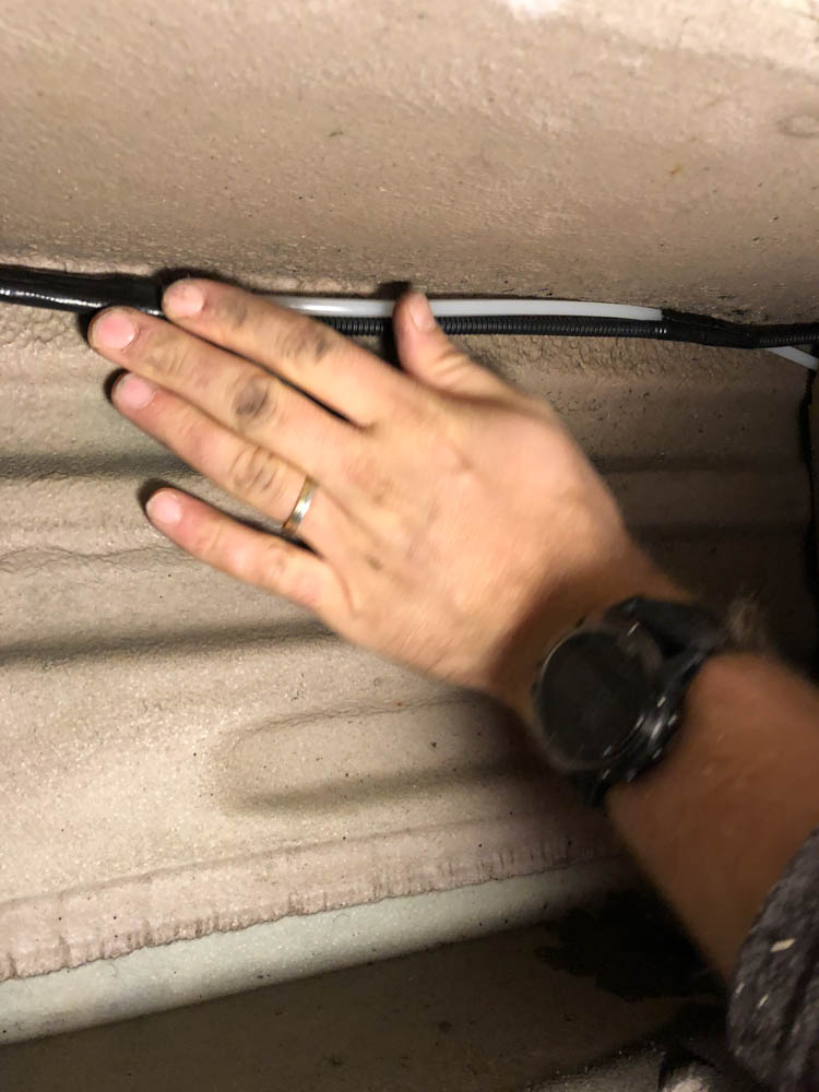 Eine Hand drückt die Diesel und Stromleitung unter dem Auto in eine Kante und zurrt sie mit einem Kabelbinder fest.