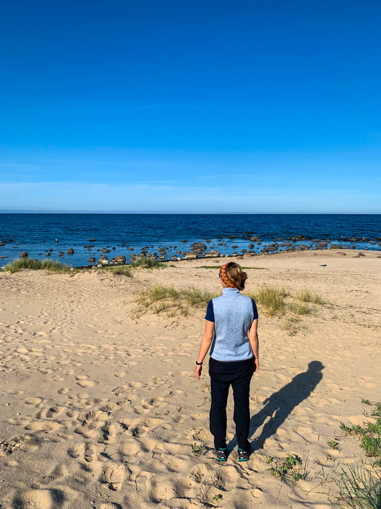 Melanie steht auf Sand und blickt auf die Ostsee vor ihr. Der Himmel ist kräftig blau