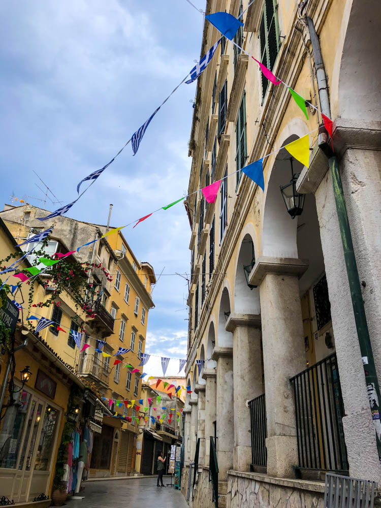 Eine Gasse in Korfus Altstadt. Es sind mehrer Wimpelgirlanden über die Gasse gespannt. Ein paar sind bunt, der Rest hat die Farben der Griechischen Nationalfahne.